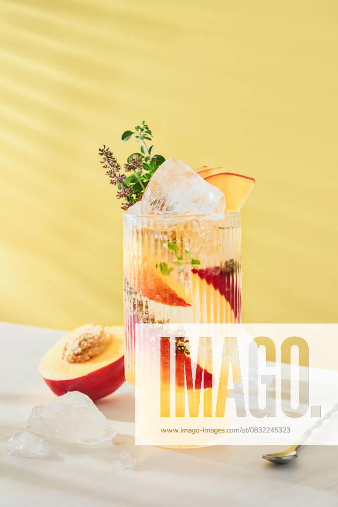 Kalter erfrischender Pfirsich-Limetten-Cocktail garniert mit Minze und Thymianblättern im Glas auf gelbem hellem Hintergrund. Sommergetränke für zu Hause. Kalter erfrischender Pfirsich-Limetten-Cocktail garniert mit Minze und Thymianblättern im Glas auf gelbem hellem Hintergrund. Sommergetränke für zu Hause. (License=RF)