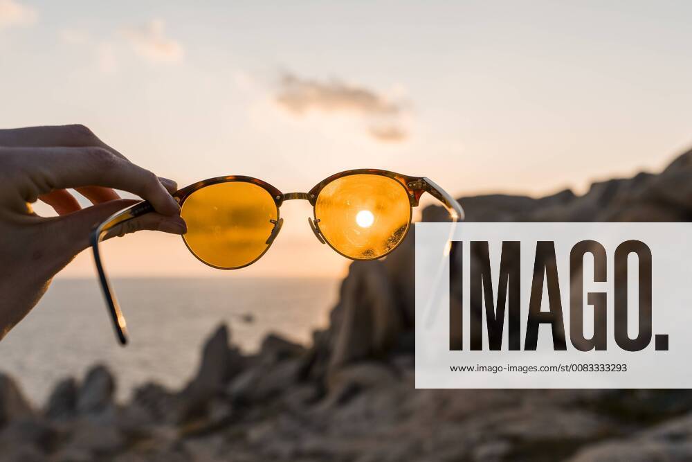 IMAGO Creative, Jahreszeit Sommer, Sonnenschutz Man s hand holding sunglasses in front of evening sun, close-up model released Symbolfoto AFVF00411