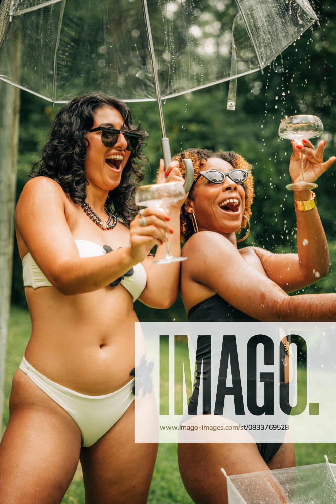 IMAGO Creative, Lifestyle, Feste im Garten #2 Two women in swimsuits laugh under umbrella with champagne splashes North Reading, Massachusetts, United States CR_FKNH250911-1827941-01 ,model released, Symbolfoto