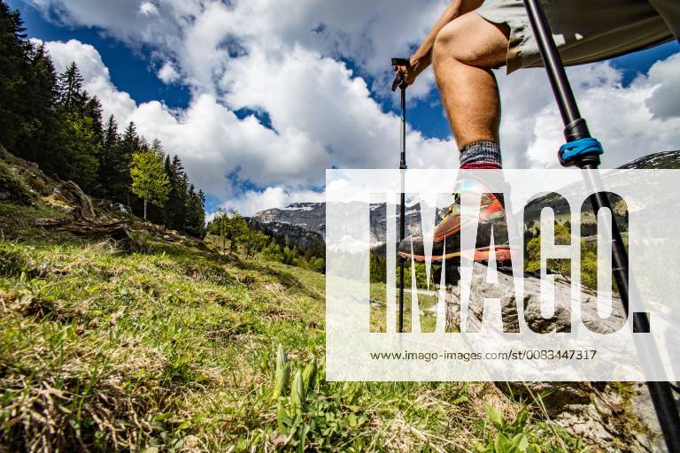 IMAGO Creative: Sommer, In den Bergen Bein eines Wanderers, mit Bergschuh und Stöcken auf Stein im Gebirge - Leg of a Mountain Hiker, with Shoe and Walking Poles, on Rock in the Mountains
