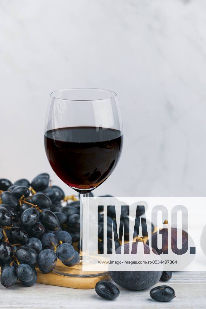 Ein Glas Rotwein mit Trauben und Feigen auf einem Holzbrett, heller Hintergrund A glass of red wine with grapes and figs on a wooden board, light-coloured background