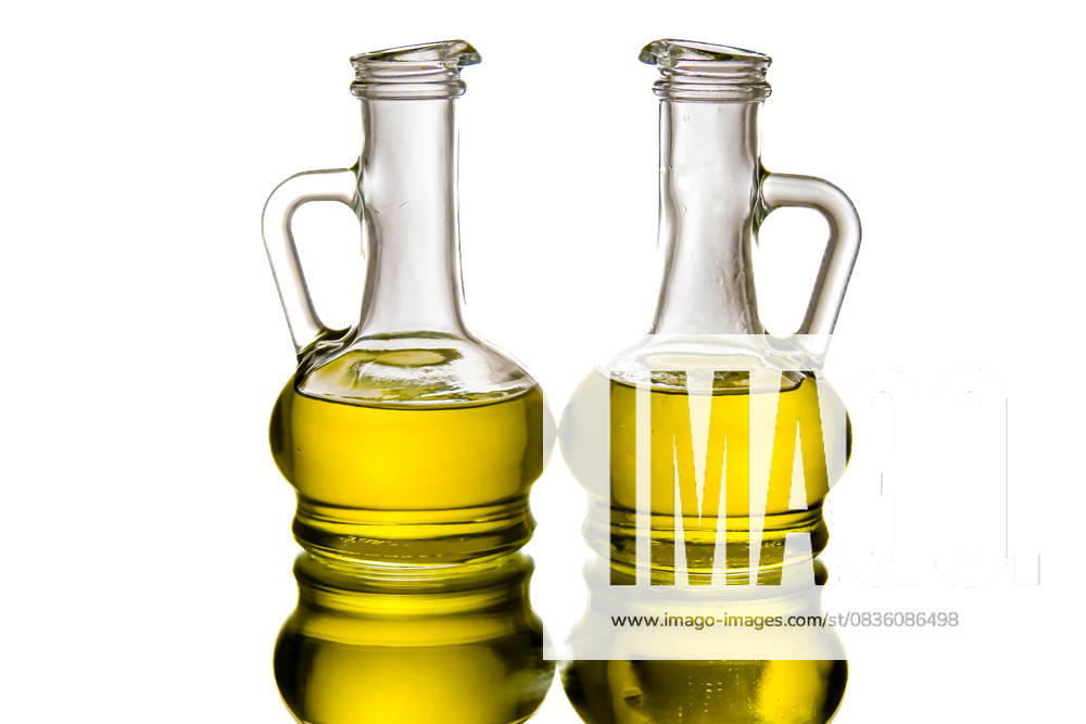 Two glass bottles filled with olive oil, placed side by side on a reflective surface, against white background and studio light. Two glass bottles filled with olive oil, placed side by side on a reflective surface, against white background and studio light., 60934994.jpg RECORD DATE NOT STATED
