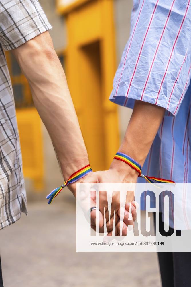 Männliches Paar, das seine Liebe und Unterstützung füreinander zeigt, indem es sich mit Regenbogenflaggen Armbändern an den Händen hält, die ihren lgbtq Plus Stolz und ihre Beziehung vor einem leuchtend gelben Hintergrund symbolisieren Male couple showing love and support for each other by holding hands with rainbow flag bracelets, symbolizing their lgbtq plus pride and relationship against a vibrant yellow background
