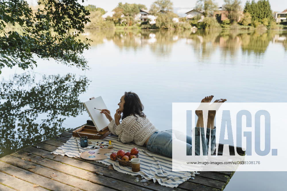 Person painting and relaxing on dock by scenic lake outdoors model released, Symbolfoto, NDEF02897