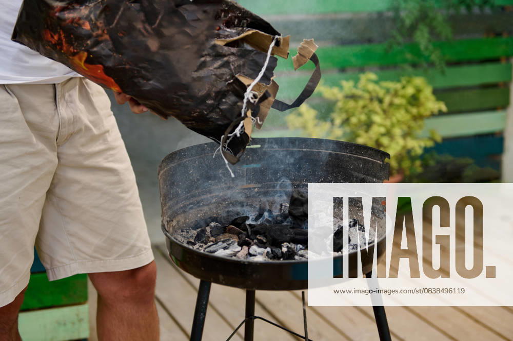 Outdoor barbecue preparation with person adding charcoal to the grill Person adding charcoal to an outdoor barbecue grill, preparing for a cookout. Relaxed and casual atmosphere in a backyard setting., model released, , property released, , 61018278.jpg RECORD DATE NOT STATED