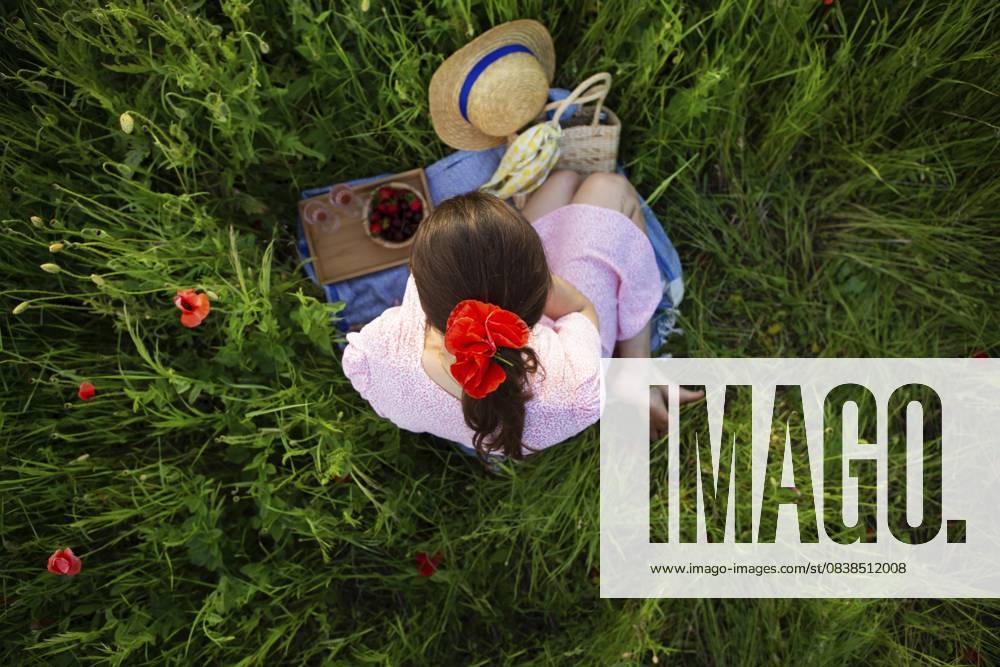 Eine junge Frau genießt ein ruhiges Picknick inmitten eines lebendigen Mohnfeldes, umgeben von der Schönheit der Natur A young woman enjoys a tranquil picnic amidst a vibrant poppy field, surrounded by nature s beauty