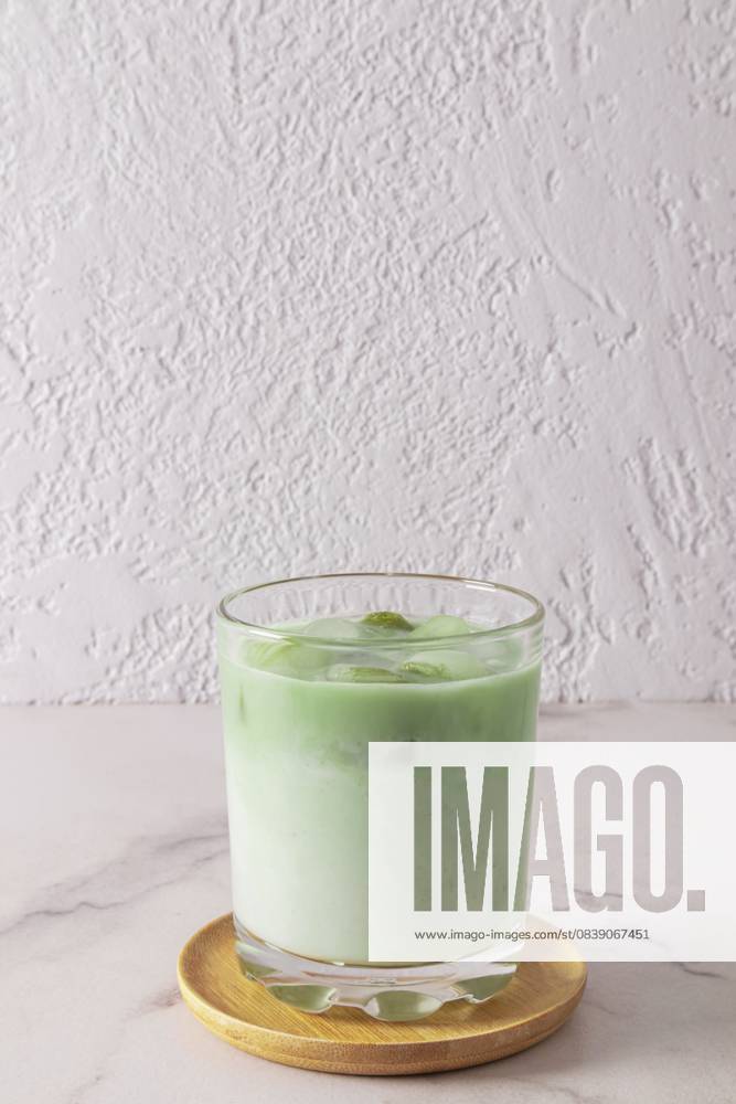 Ein großes Glas natürlichen Grüntee Matcha Latte steht auf einem Holzteller und einem weißen Marmortisch. Gesundheitsförderndes, belebendes Mittel A wide glass of natural green tea matcha latte stands on a wooden plate and a marble white table. health-improving, invigorating agent
