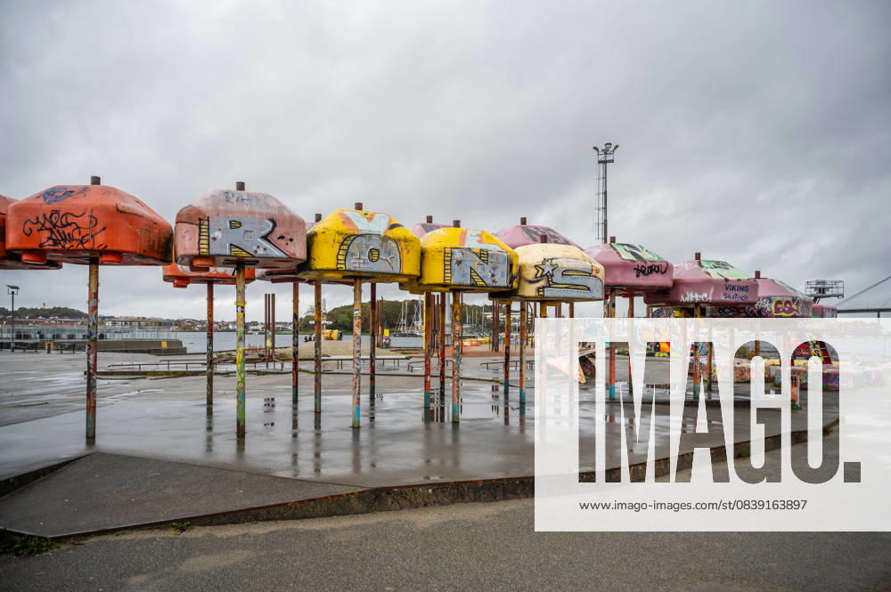 IMAGO Creative, Jahreszeit Sommer, Regen, Sommerregen Eine Reihe bunter, mit Graffiti beschmierter Regenschirme mit der Aufschrift ROONS steht in einem verlassenen Hafengebiet unter einem bewölkten Himmel, Stavanger, Norwegen A row of colorful, graffiti-covered umbrellas spelling ROONS stands in an abandoned waterfront area under a cloudy sky, Stavanger, Norway (License=RM)