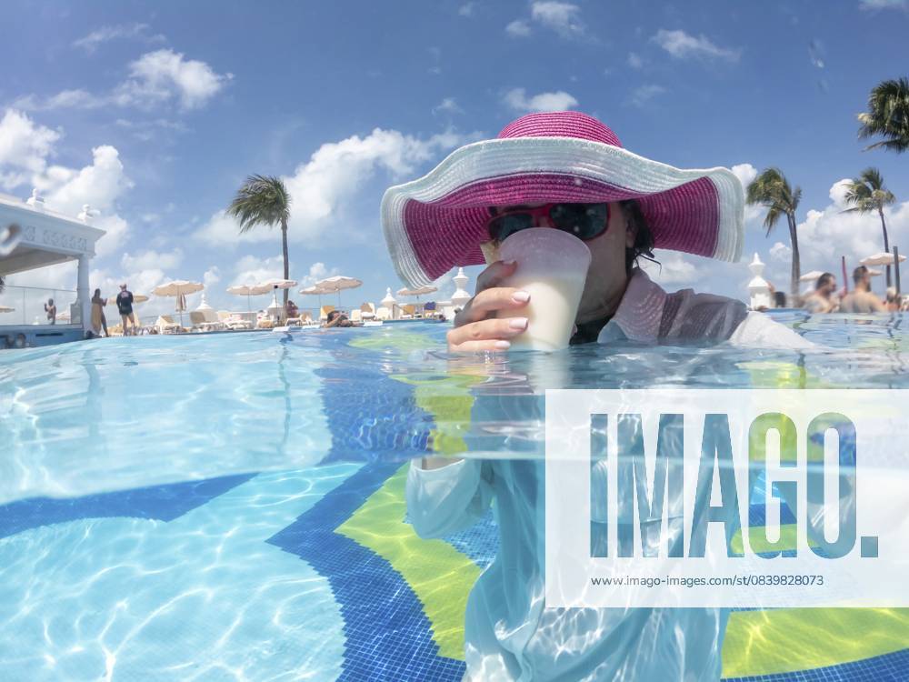 Frau mit Hut steht im Pool und trinkt Cocktail. Konzept eines schönen Urlaubs Woman wearing hat staning in pool drinking cocktail. Concept of happy vacation