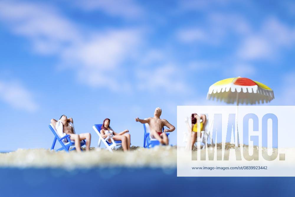 Miniaturmenschen beim Sonnenbaden am Strand mit blauem Himmelshintergrund, Sommerzeitkonzept Miniature people sunbathing on The beach with blue sky background, Summer time concept
