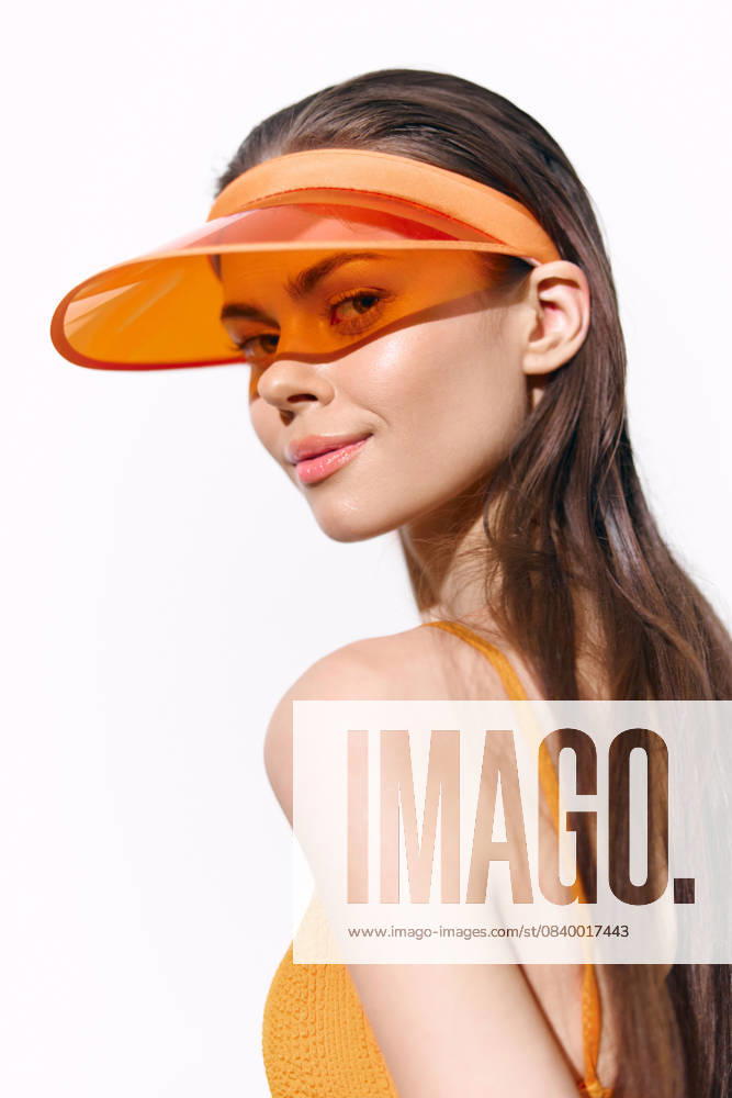 Young woman wearing an orange visor, showcasing her playful smile and confidence against a clean white background, perfect for summer fashion concepts. Stylish young woman in an orange visor exuding confidence and summer vibes, ideal for fashion and lifestyle themes, set against a minimalist white background., model released, , 98075224.jpg RECORD DATE NOT STATED