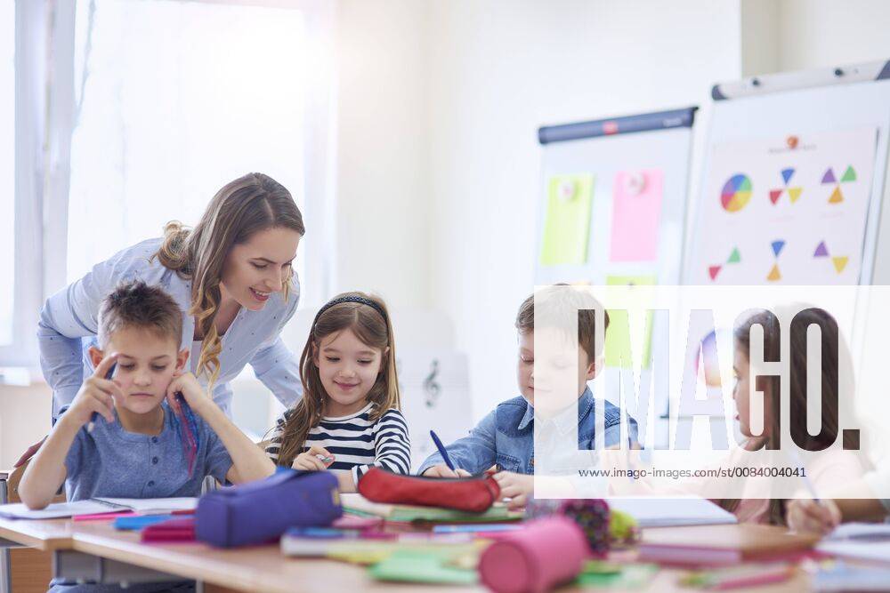 IMAGO Creative: Gesellschaft, Schule, Schulanfang Smiling teacher helping pupils with their tasks in class model released Symbolfoto property released ABIF00378
