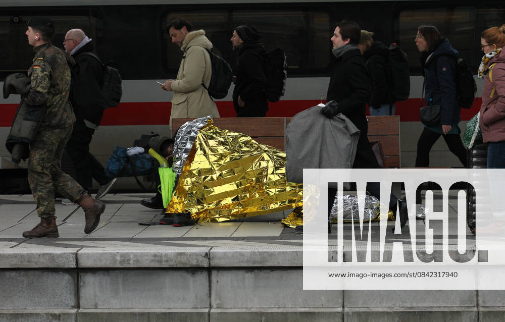 Ein Obdachloser liegt auf einer Sitzbank auf dem Bahnsteig im Hauptbahnhof Hamburg. Reisende gehen an ihm vorbei. St. Georg Hamburg