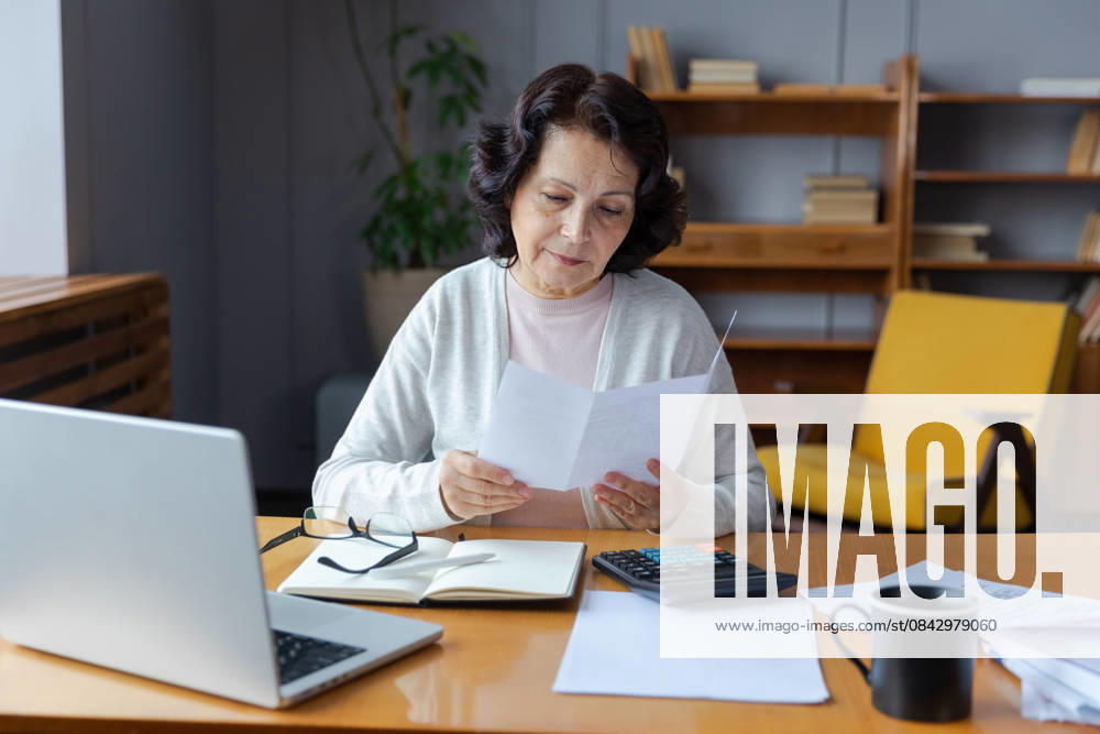Middle aged senior Frau sitzen mit Laptop und Papier Dokument, Pensive ältere reife Dame Lesen Papier Rechnung zahlen online zu Hause verwalten Bank Finanzen Berechnung Steuern Planung Darlehen Schulden Rente Zahlung Middle aged senior woman sit with laptop and paper document. Pensive older mature lady reading paper bill pay online at home managing bank finances calculating taxes planning loan debt pension payment (License=RF) ,model released, Symbolfoto