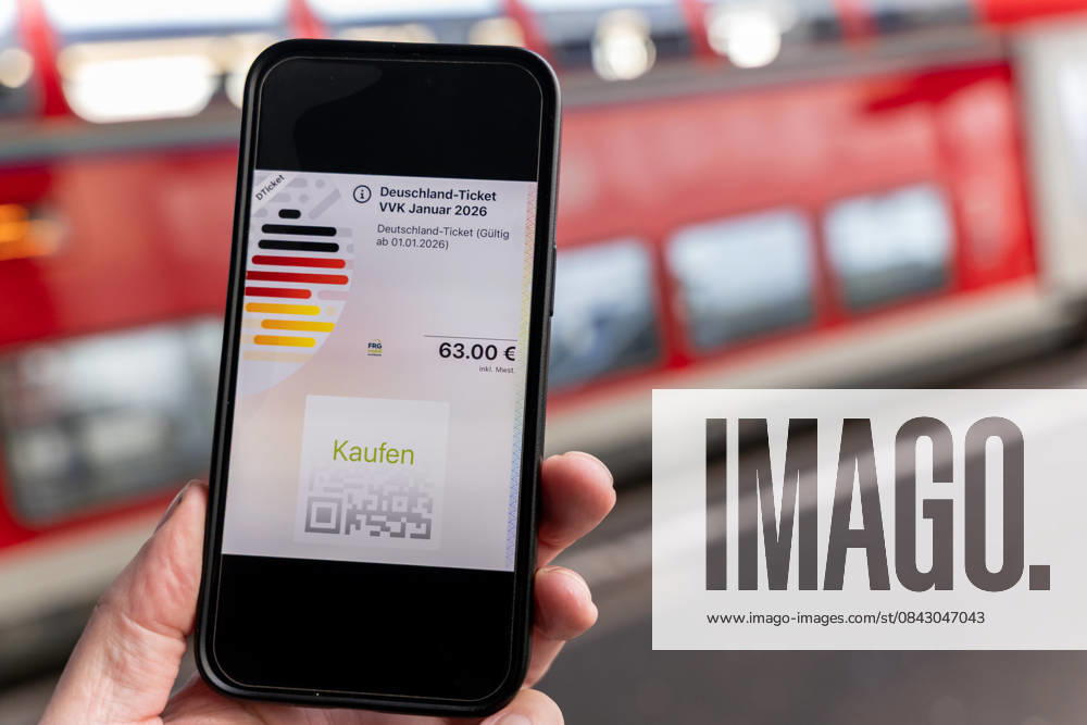 Deutschlandticket mit neuem Preis am Bahnhof 17.12.25, Limburg: Symbolfoto, Illustrationsbild, Symbolbild, Illustrationsfoto, Alltagsszene Ein Smartphone zeigt das digitale Deutschlandticket mit einem Preis von 63 Euro. Das Mobiltelefon wird auf einem Bahnsteig gehalten, im Hintergrund ist ein roter Zug unscharf zu sehen. Das Bild steht im Zusammenhang mit der geplanten Preiserhöhung des Deutschlandtickets zum 1. Januar 2026 sowie mit dem öffentlichen Nahverkehr und dem Bahnverkehr in Deutschland. Limburg Hessen