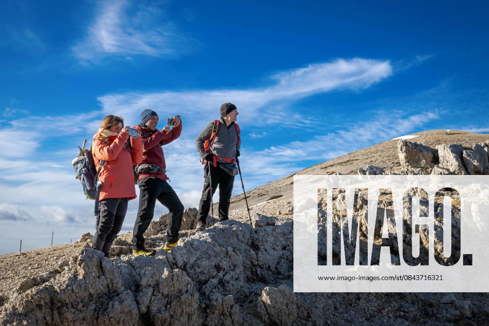 Hikers on a mountain trail. Guarcino (FR), Italy - December 21, 2025: Three hikers on a rocky mountain peak enjoy photographing the surrounding landscape with their smartphones. Guarcino FR Italy