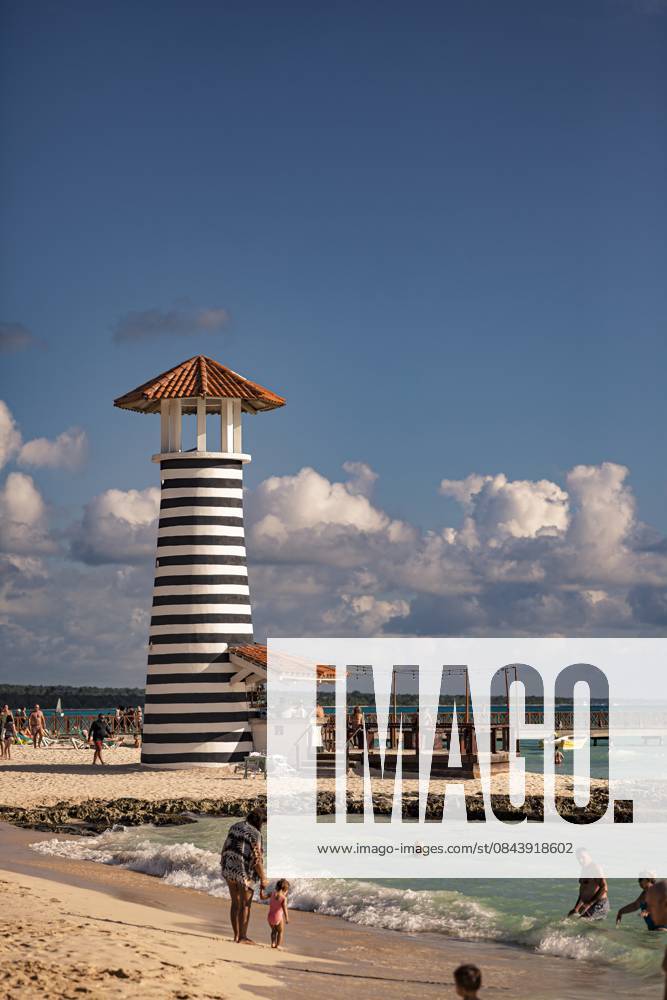 Tourists enjoying dominican republic beach with iconic striped lighthouse Bayahibe, Dominican Republic 1 January 2025: Tourists relaxing on the beach near a black and white striped lighthouse in dominicus, dominican republic, a popular caribbean destination, 64091164.jpg RECORD DATE NOT STATED