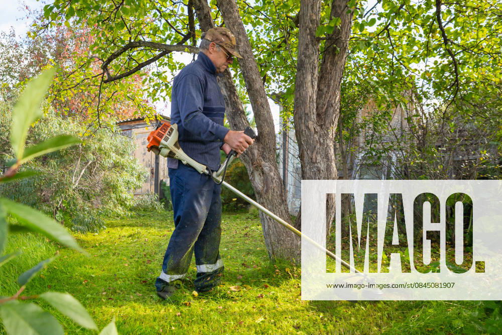Senior man uses grass trimmer to cut overgrown lawn in his backyard Chelyabinsk, Chelyabinsk Oblast, Russia CR_STCJ260106-1921669-01 ,model released, Symbolfoto