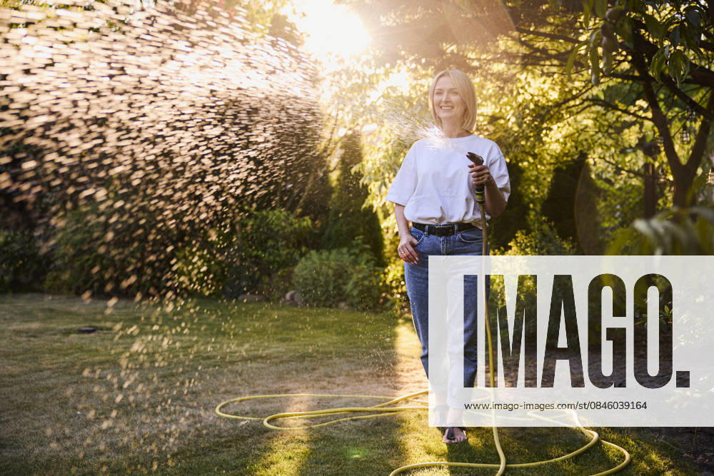 Smiling woman watering lawn with hose outdoors at sunset in summer model released, Symbolfoto property released, BSZF02960