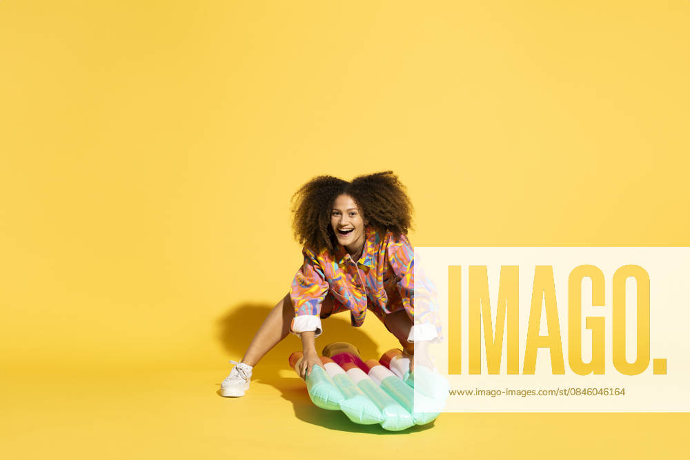 Woman with curly hair holding ice cream shaped pool raft against yellow background model released, Symbolfoto, MIKF00572