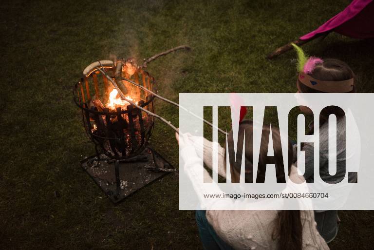 Two girls wearing feather headdress, grilling sausage over camp fire model released Symbolfoto property released MOEF01217