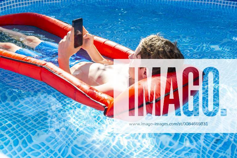 Boy floating on water in swimming pool using smartphone model released Symbolfoto SARF03779