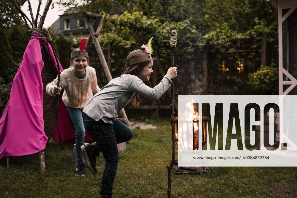 IMAGO Creative: Digitale Welt, Verzicht auf Technologie Two girls wearing feather headdress, dancing with twist bread around the camp fire model released Symbolfoto property released MOEF01214