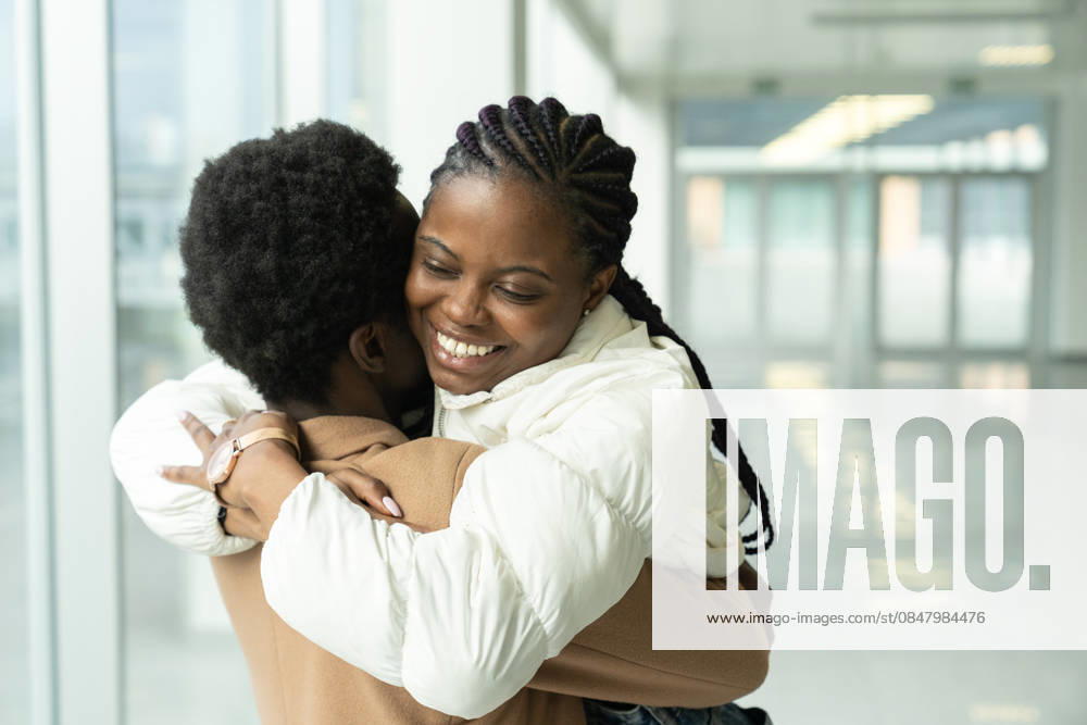 Wiedersehen eines Paares am Flughafen: Afrikanische Frau umarmt ihren Freund, der nach einem Urlaub oder einer Auslandsreise zurückkehrt. Couple reunion in airport: portrait of happy african american female met hug boyfriend arriving from vacation trip abroad. (License=RF) ,model released, Symbolfoto