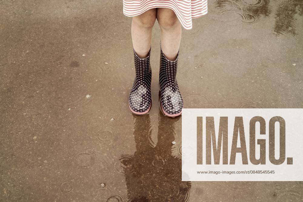 Kind in Regenstiefeln läuft in eine Pfütze Child wearing rain boots walking into a puddle