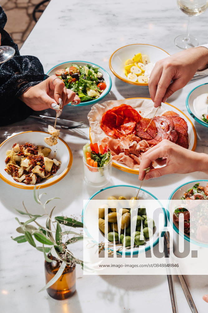 IMAGO Creative, Food, Tapas Unrecognizable hands enjoying a vibrant Mediterranean feast Cropped unrecognizable hands enjoy a Mediterranean meal with a variety of plates including olives, cured meats, salad, and artichokes on a white marble table. Model Released Andrerako_ID32184_1095647_002