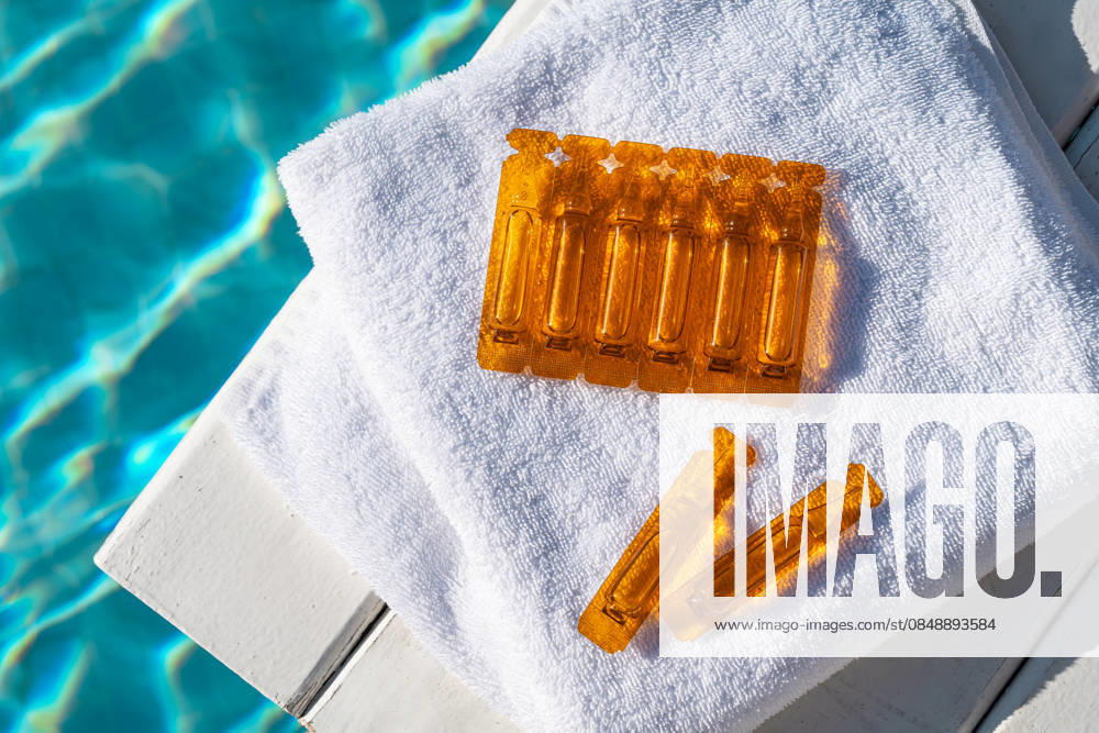 Hair care oil ampoules on a towel by the pool Orange hair care oil ampoules placed on a white towel beside a shimmering pool. Ideal for smoothness and sun protection, enhancing beauty and hair health. Model Released IrinaChetverikova_ID33524_1167070_002