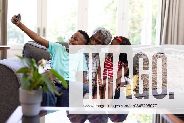 Senior African American man and his grandchildren at home Senior African American man and his grandchildren enjoying their time at home together, sitting on a couch, embracing, smiling, using a smartphone, taking a selfie, model released, , property released, Cape Town, South Africa, 19.02.2020, 1340053.jpg, people,family,grandfather,granddad,granddaughter,grandson,siblings,brother,sister,childhood,together,closeness,interacting,sitting,couch,holding,using,phone,mobile phone,smartphone,connection,communication,taking,photo,photograph,selfie,real people,home,house,domestic life,lifestyle,enjoying,free time,leisure,relaxing,weekend,summer,sunny,love Child,Girl,Female,Mixed-Race,Mid Adult,Man,Male,Black Indoors,Front view,Day,Three Quarter Le