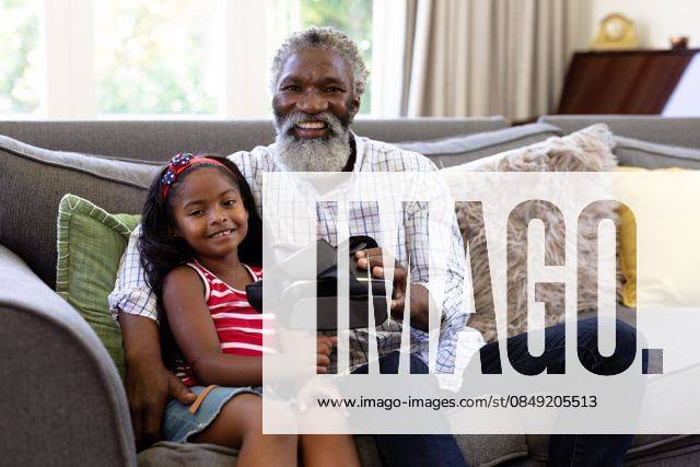 Senior African American man and his granddaughter using vr headset Senior African American man and his granddaughter enjoying their time at home together, sitting on a couch, holding a VR headset, looking at the camera and smiling, model released, , property released, Cape Town, South Africa, 19.02.2020, 1340099.jpg, people,family,grandfather,granddad,granddaughter,childhood,together,closeness,interacting,sitting,couch,happy,smiling,holding,vr,virtual reality,headset,connection,communication,real people,home,house,domestic life,lifestyle,enjoying,free time,leisure,relaxing,weekend,summer,sunny,love Child,Girl,Female,Mixed-Race,Mid Adult,Man,Male,Black Indoors,Side view,Looking at camera,Day,Three Quarter Length