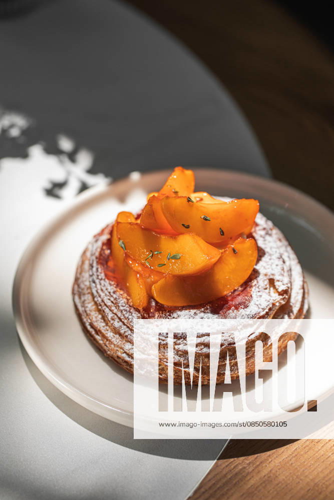Pfirsich-Plundergebäck mit Puderzucker Flaky danish pastry topped with fresh peach slices and powdered sugar served on plate (License=RF)