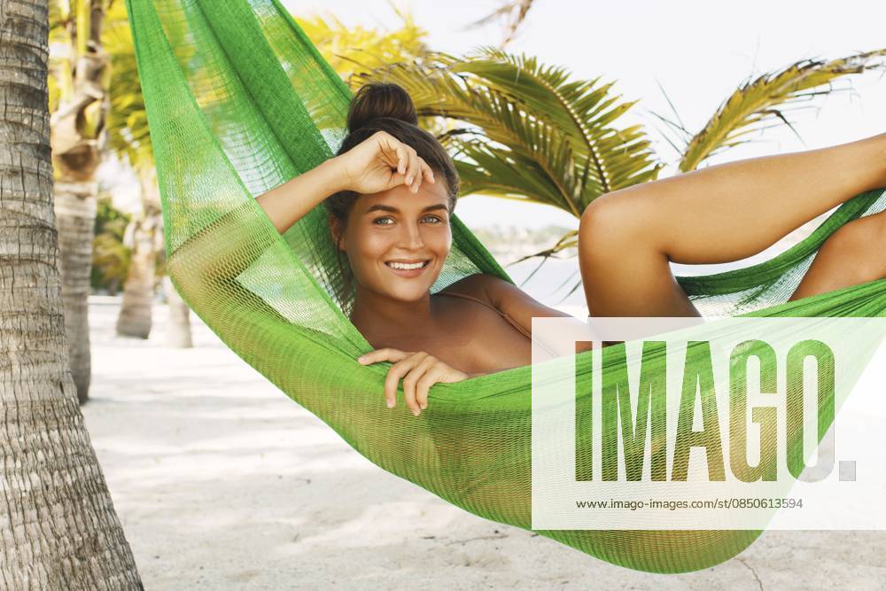 Glückliche und schöne Frau, die in der Hängematte am Strand mit einem wunderschönen weißen Sand liegt Happy and beautiful woman lying in the hammock on the beach with a wonderful white sand