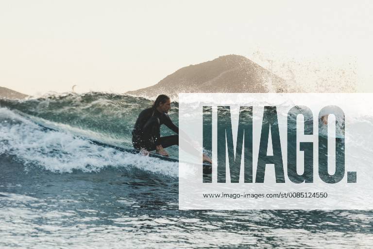 Side view shot of longboard surfer in wetsuit riding wave in sea at sunset, Tenerife Canary Islands Spain VISE003723 model released Symbolfoto