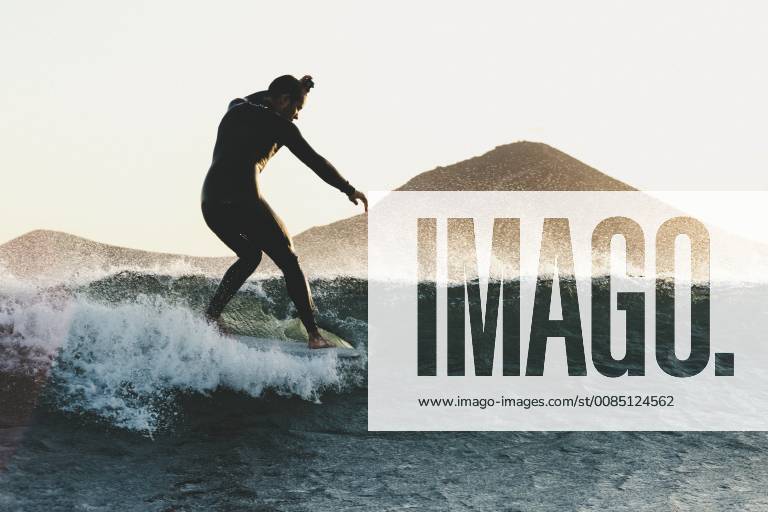 Side view shot of longboard surfer in wetsuit riding wave in sea at sunset, Tenerife Canary Islands Spain VISE003738 model released Symbolfoto