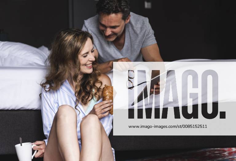 Happy couple in bedroom at home with tablet, coffee and croissant model released Symbolfoto UUF14388