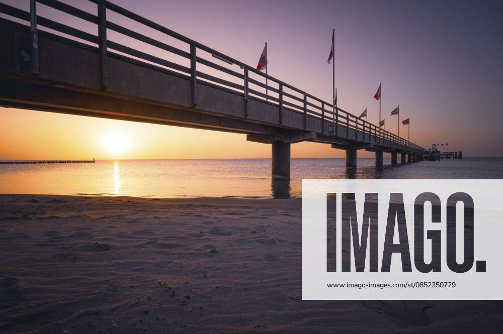 Ein Pier im Licht eines Sonnenaufganges über dem ruhigen Meer mit violettem Himmel, der Blick über den Sandstrand entlang der Seebrücke auf die Ostsee, Südstrand in 23775 Großenbrode, Deutschland A pier in the light of sunrise over the calm sea with purple sky, the view across the sandy beach along the pier to the Baltic Sea, Südstrand in 23775 Großenbrode, Germany