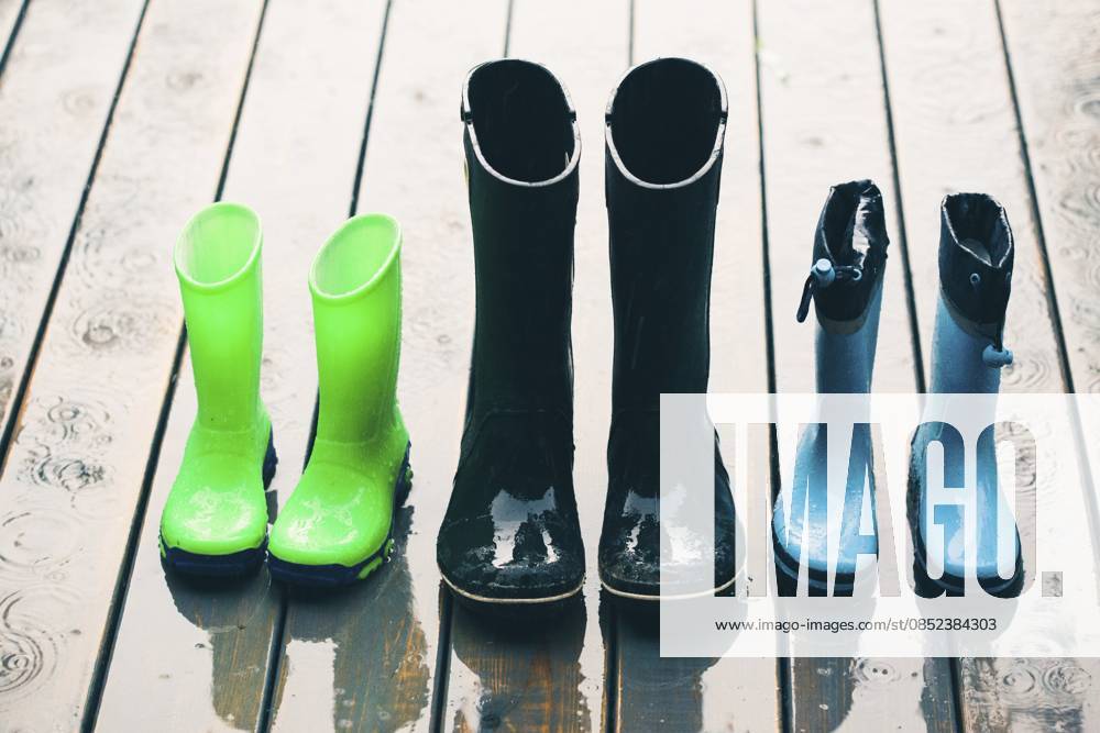 Reihe von Gummistiefeln in verschiedenen Größen, die bei Regen auf einer Holzveranda stehen Row of wellies in various sizes standing on a wooden porch while raining
