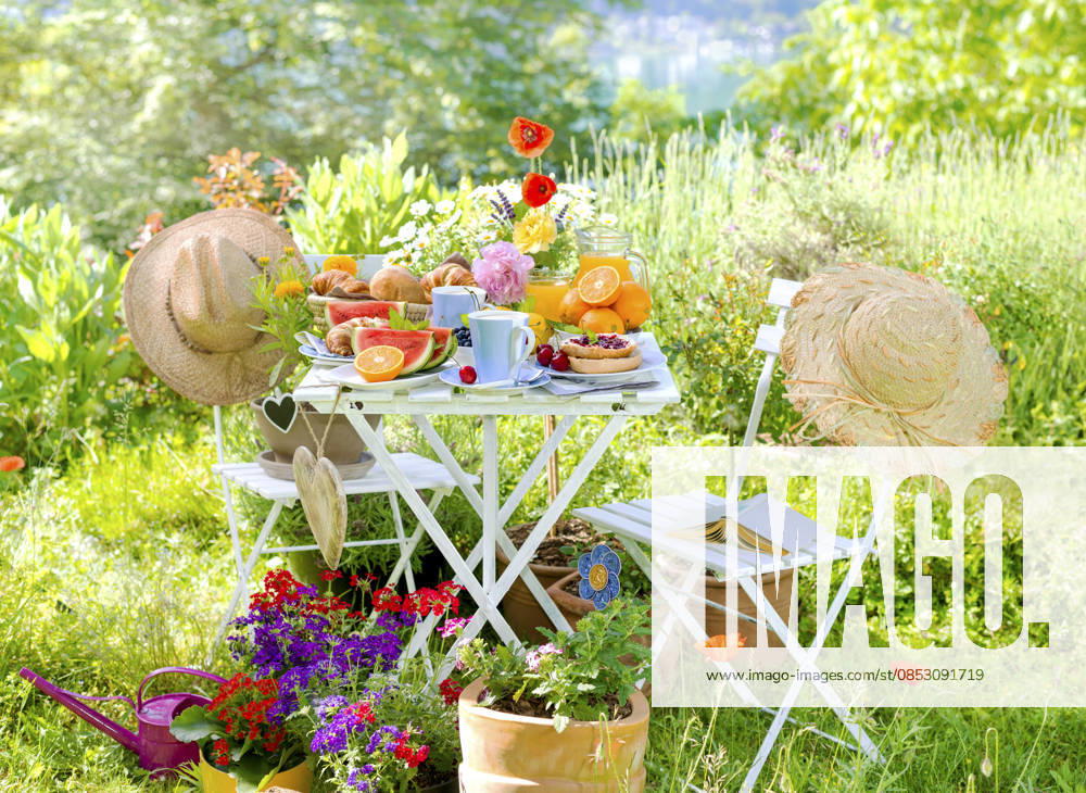 Fruehstueck fuer zwei, angerichtet auf einem Tisch im bunt bluehenden Garten am See mit Sonnenhueten und Herzen, Composing Breakfast for two, served on a table in a colorful garden blooming with coneflowers and hearts, Composing BLWS745584