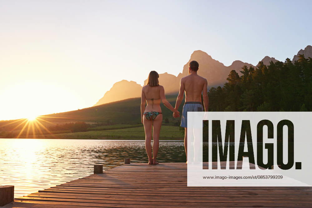 Rearview shot of a young couple in swimsuits standing on a dock at sunset. (License=RF) ,model released, Symbolfoto