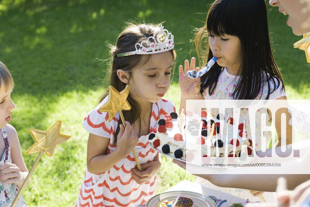 Girl blowing out candles on birthday cake at outdoor birthday party