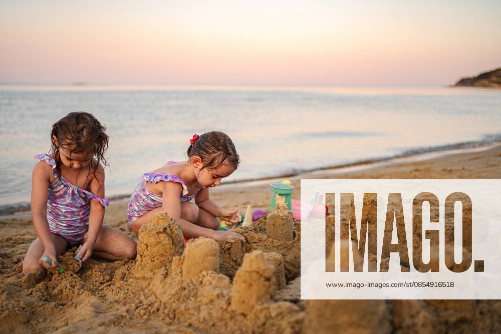 Sandburg-Abenteuer bei Sonnenuntergang mit der Familie am Meeresufer Two young siblings joyfully building sandcastles on a serene beach at dusk. (License=RF) ,model released, Symbolfoto