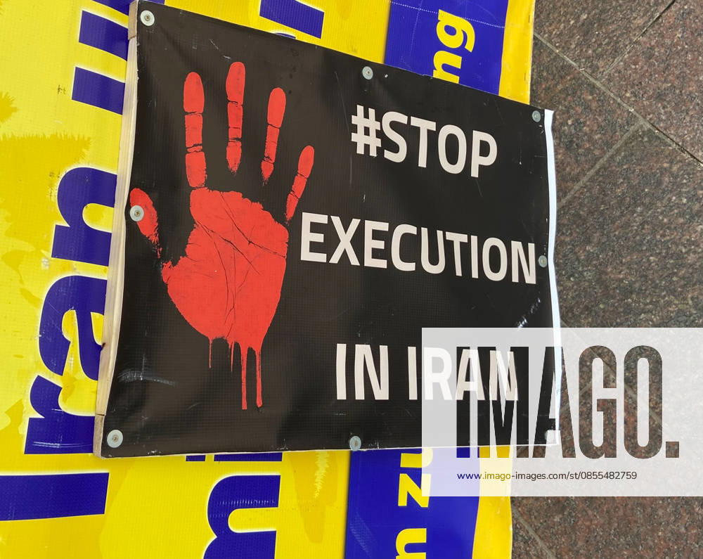 Flensburg, Schleswig-Holstein Zu sehen ist ein schwarzes Protestplakat mit roter Handfläche und der Aufschrift STOP EXECUTION IN IRAN, befestigt vor einem gelben Banner. Die Bildsprache ist klar, direkt und auf visuelle Aufmerksamkeit ausgelegt; sie verweist auf Menschenrechtsverletzungen, Todesstrafe und internationalen Protest. Aufnahme vom 02.05.2026, Flensburg
