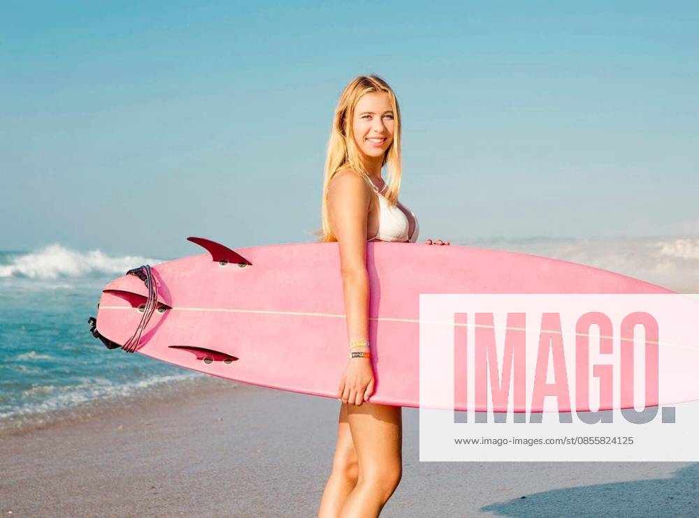 A beautiful surfer girl looking at the beach with her surfboard model released Symbolfoto
