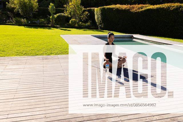 Asian female meditating on yoga mat at wooden pool deck, shorts, bottle, phone, copy space, model released, property released, 10.04.2025 06:00:00, 11794285