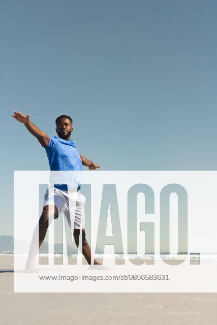 African American man standing barefoot on sandy beach at waterline wearing blue shirt white shorts, model released, property released, 27.03.2025 06:00:00, 12885004