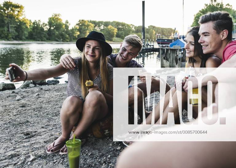 Group of friends sitting together having a barbecue and taking a selfie at the riverside model released Symbolfoto UUF14841