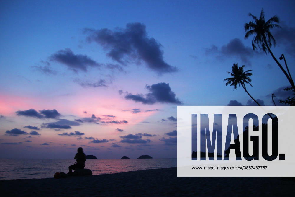 Ein unbekannter Mann sitzt bei Sonnenuntergang auf den Steinen an einem Sandstrand in Meeresnähe. Koh Chang, Thailand. Unrecognizable man is sitting on the stones at the sunset on a sandy beach near to sea. Koh Chang, Thailand. (License=RF)